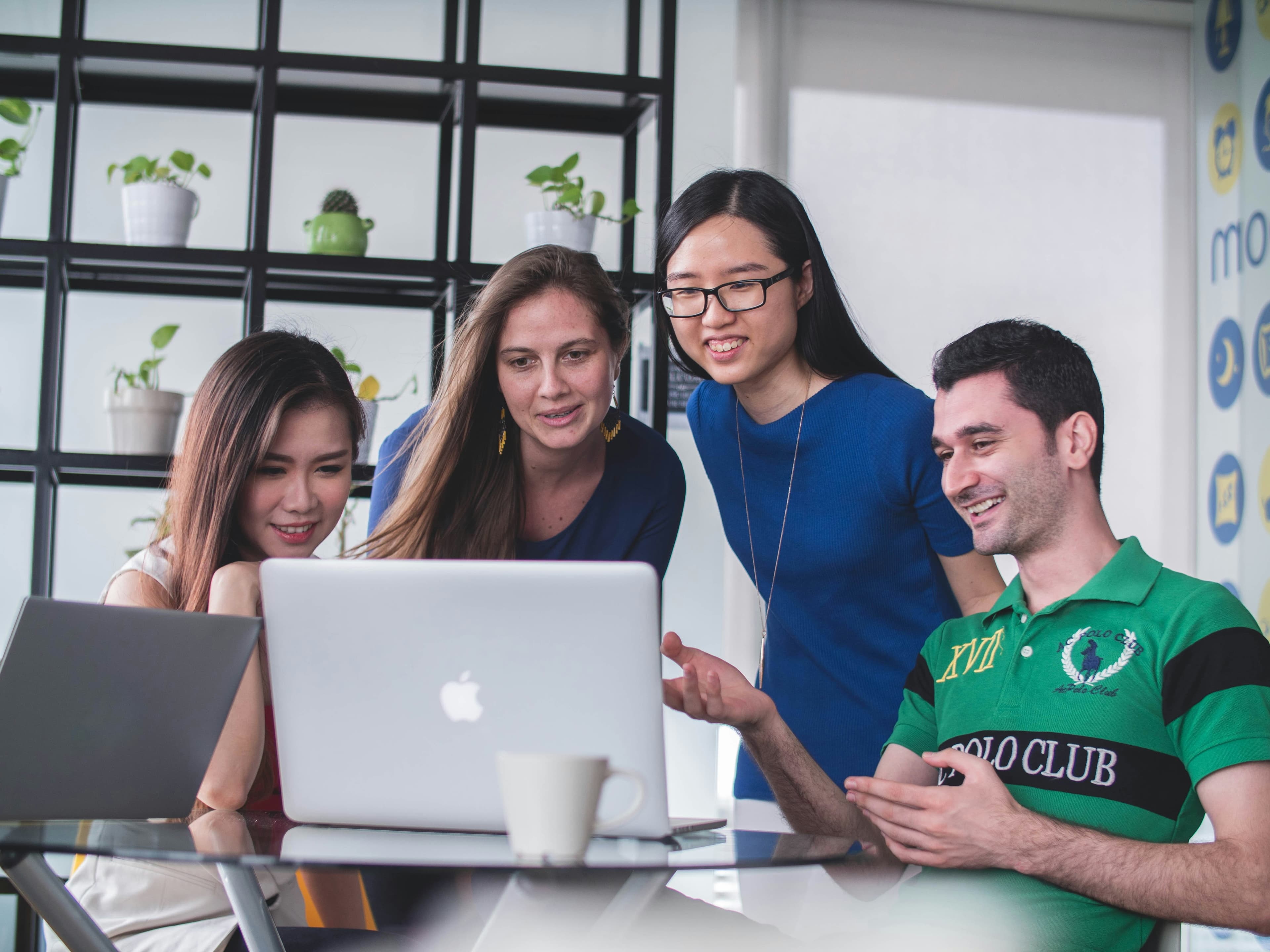 A diverse team gathered around a laptop, discussing work together